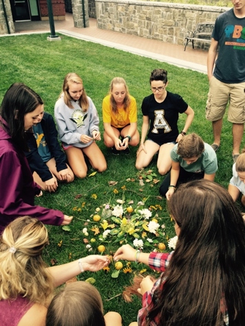 Set-the-Stage Activity - Students are seated in the grass in a circle creaking a mandala using flowers, leaves and leaves.