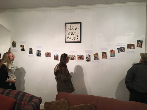Viewers are looking at the works created by students. The work is hung on a white wall on a long wire attached with clips.